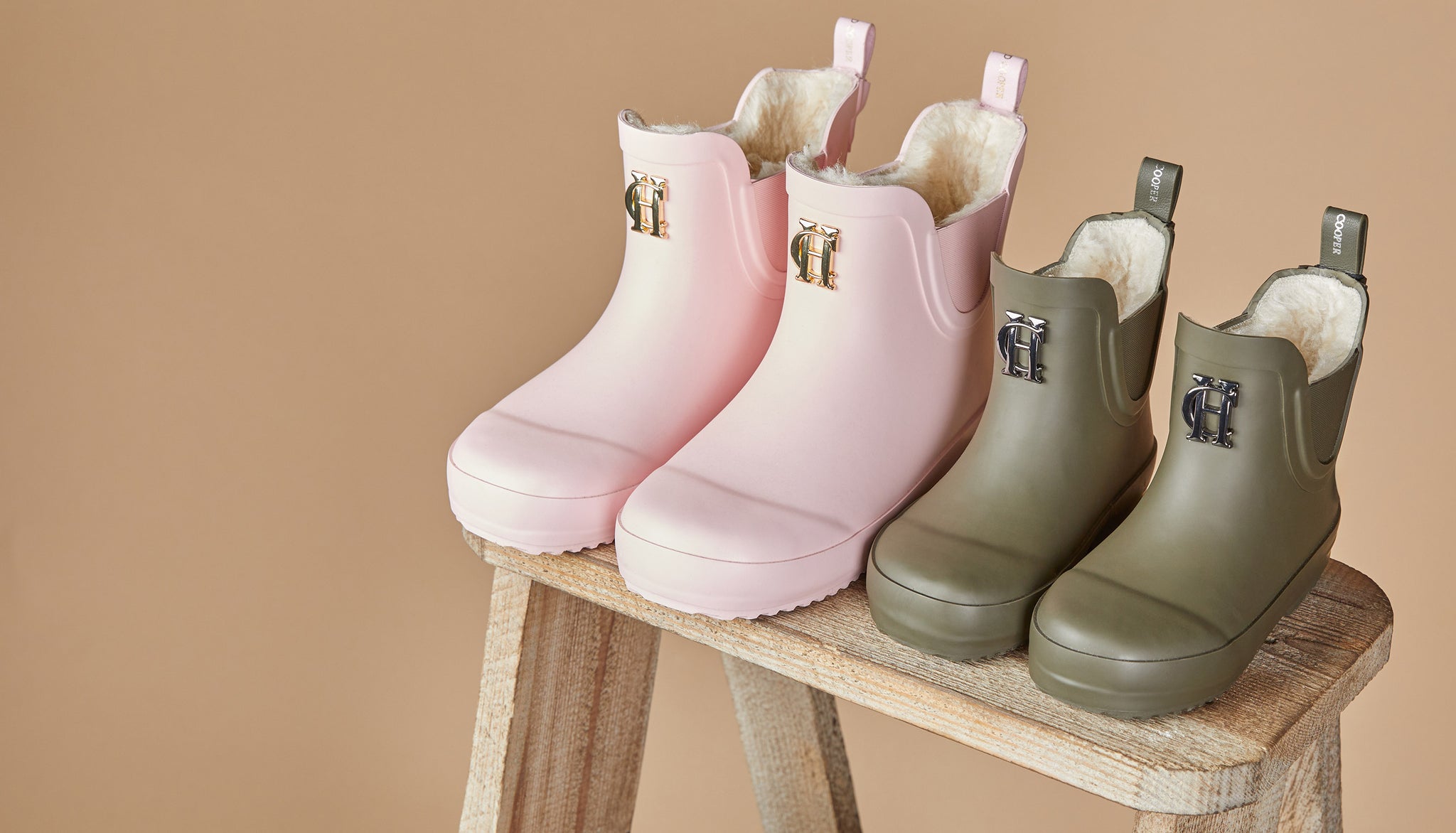 Two pairs of children's wellingtons in pink and green with sherpa lining sat on a stool